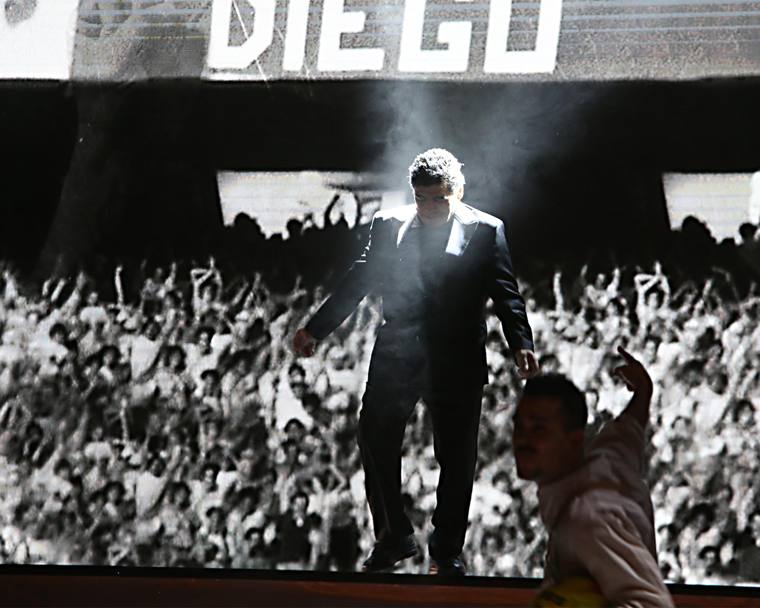 Maradona sale sul palco del San Paolo mentre alle spalle scorrono le immagini dei trionfi degli anni Ottanta.